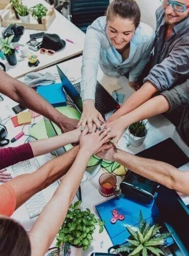 Un gruppo di lavoro unisce le mani sopra il tavolo: il piano si costruisce insieme
